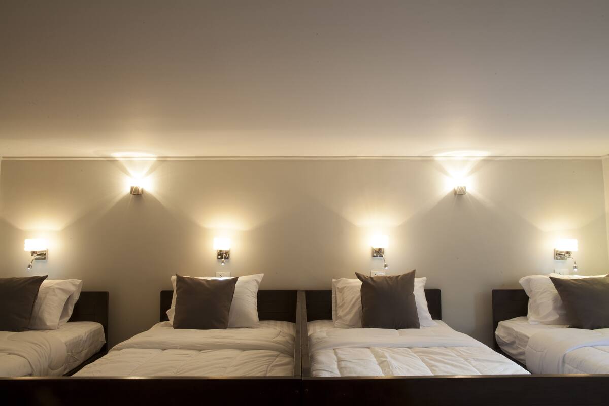 Habitación de hotel con cuatro camas individuales, cada una con cabecera y lámparas de noche.