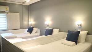 Et hotelværelse med tre senge, hver med pude og dyne. Der er vægmonterede lamper på hver side af sengene.