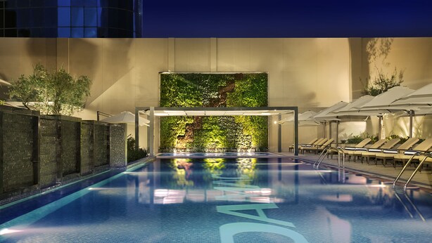 An indoor swimming pool with a tiled floor, a green wall with plants, and lounge chairs along the side. - DAMAC Maison Cour Jardin (Dubai)