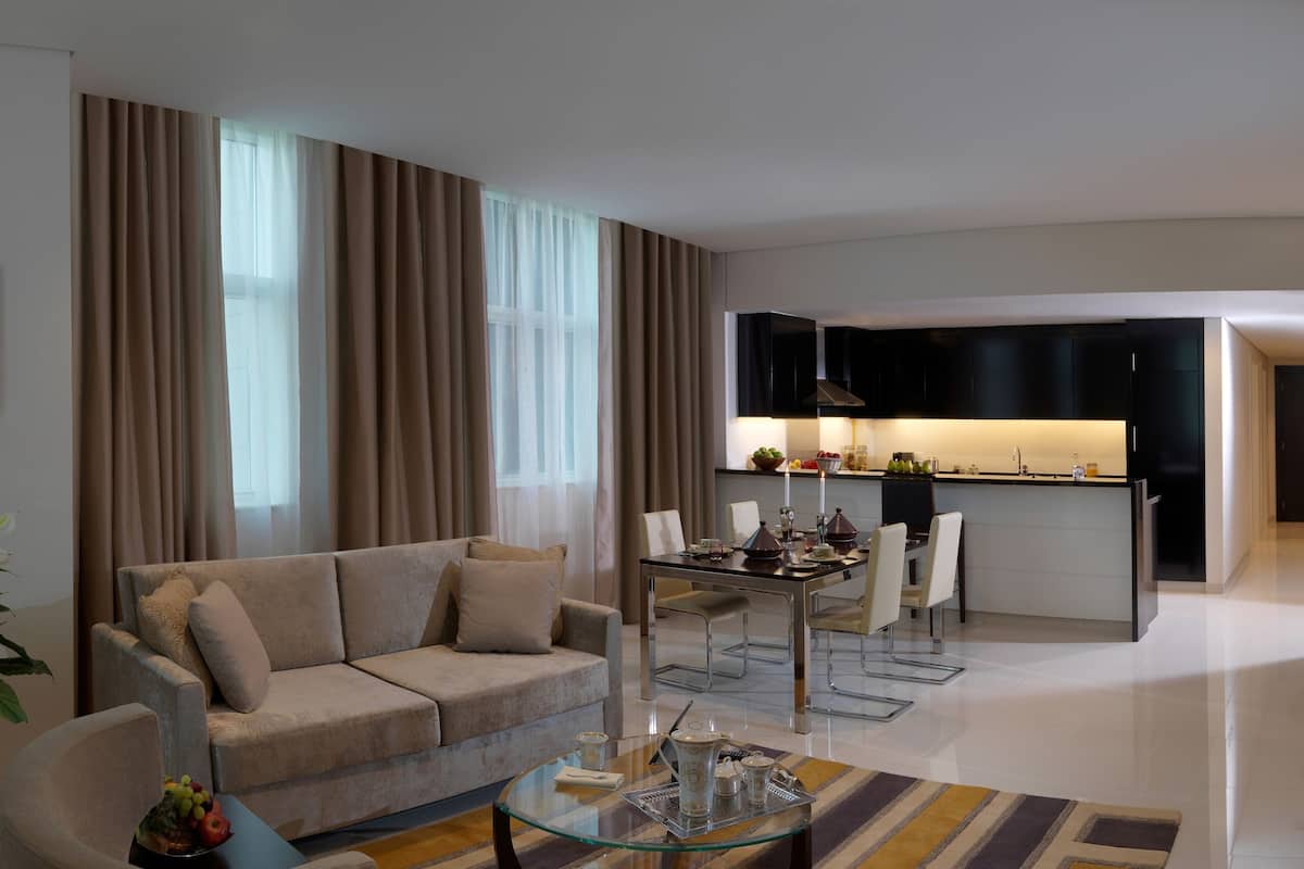 A modern living room with a sofa, a glass coffee table, and a dining area with a table set for two.