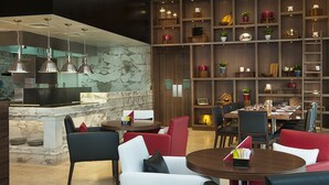 A modern restaurant with marble countertops, red and black chairs, and wooden shelves with kitchenware. - DAMAC Maison Cour Jardin (Dubai)