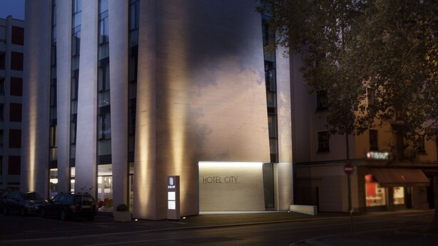 Um edifício de hotel moderno com um letreiro chamativo 'HOTEL CITY', janelas amplas e uma entrada bem iluminada.