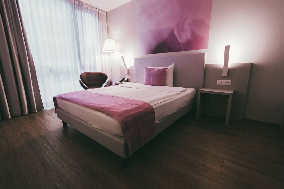 A hotel room with a bed, a chair, a nightstand, and a lamp.