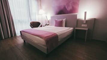 A hotel room with a bed, a chair, a nightstand, and a lamp.