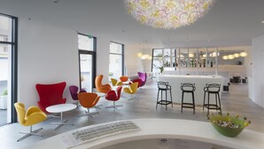 Um interior moderno com cadeiras coloridas, uma mesa branca central e um lustre decorativo.