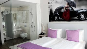 A modern hotel room with a glass shower enclosure, a bed with white and purple bedding, and a wall-mounted painting of a vintage car.