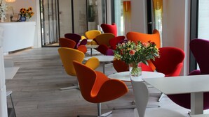 Uma sala de jantar moderna com cadeiras vibrantes em laranja e amarelo, uma mesa branca e um vaso de flores.