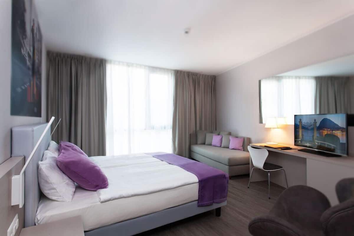 A hotel room with a bed, a desk, a chair, a sofa, and a television.