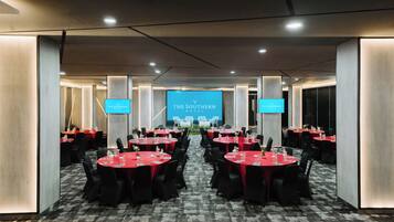Un salón de conferencias con varias mesas, sillas y una pantalla grande que muestra la marca 'The Southern Hotel'.