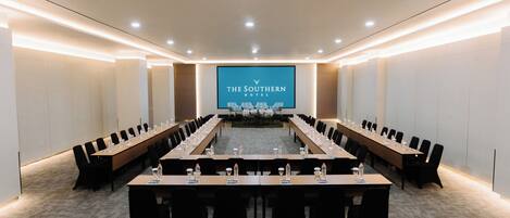 Un salón de conferencias con una mesa larga, sillas y una pantalla que muestra la marca 'THE SOUTHERN HOTEL'.