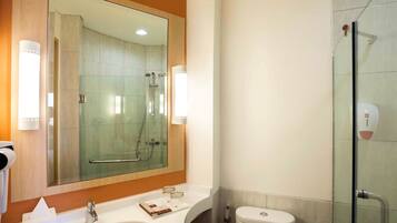 Un baño moderno con un espejo grande, un lavamanos, una cabina de ducha de vidrio y un inodoro.