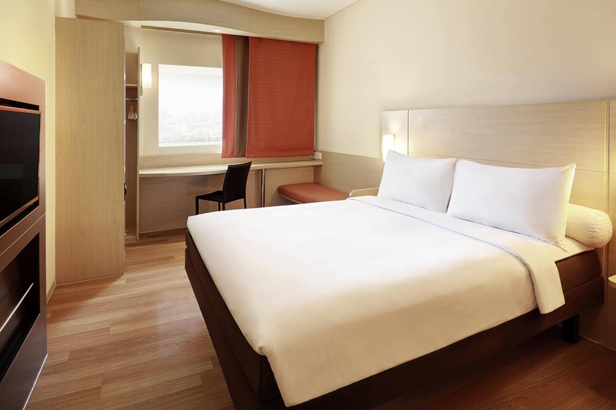 Una habitación de hotel con una cama grande, un escritorio y una televisión.