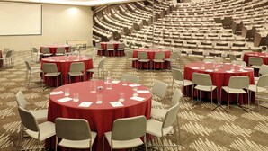 Ein Konferenzraum mit runden Tischen und Stühlen, einem Teppichboden und einem großen Auditorium im Hintergrund.
