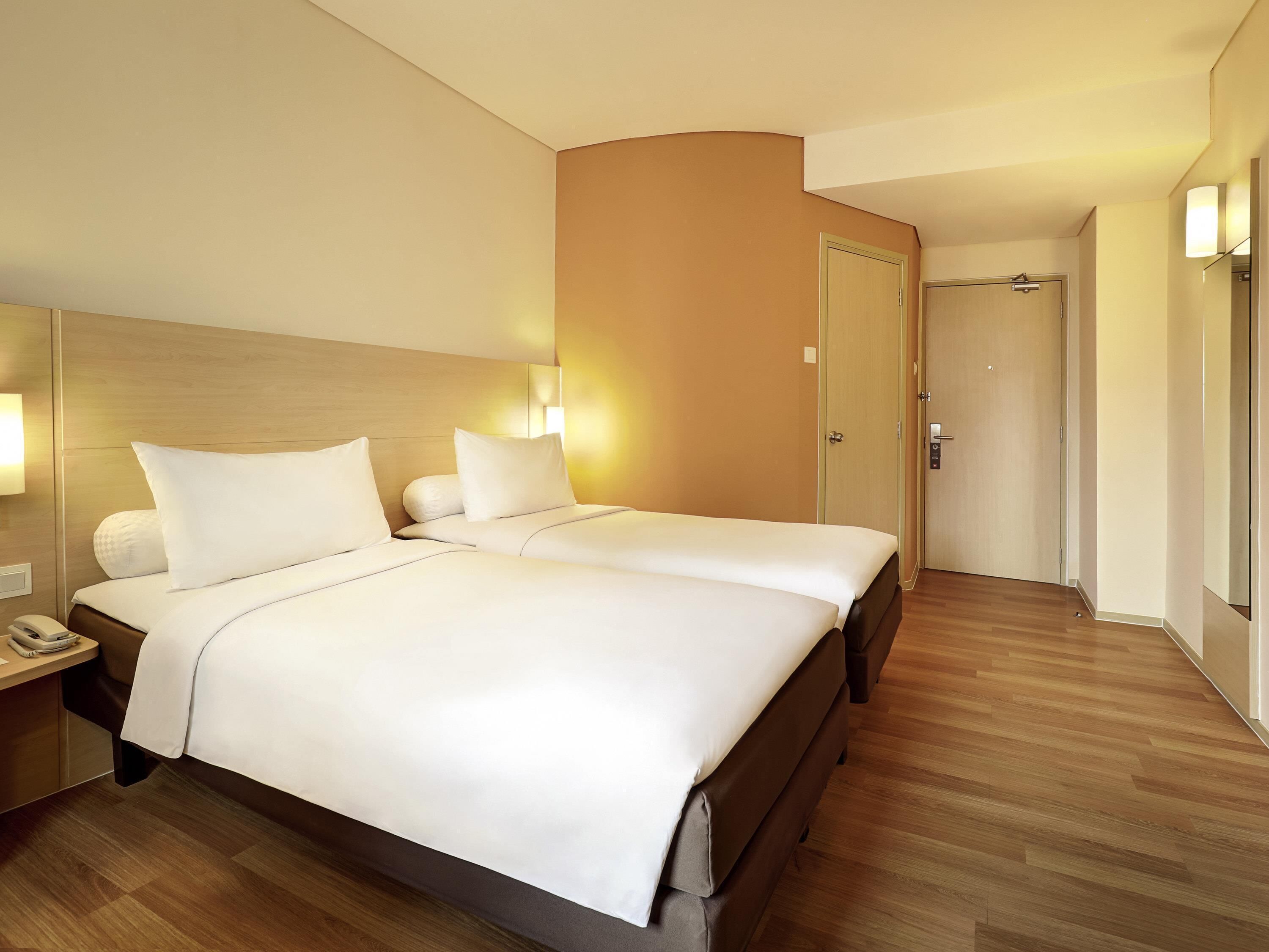A hotel room with two beds, a wooden headboard, bedside lamps, a phone on the nightstand, and a wooden floor.