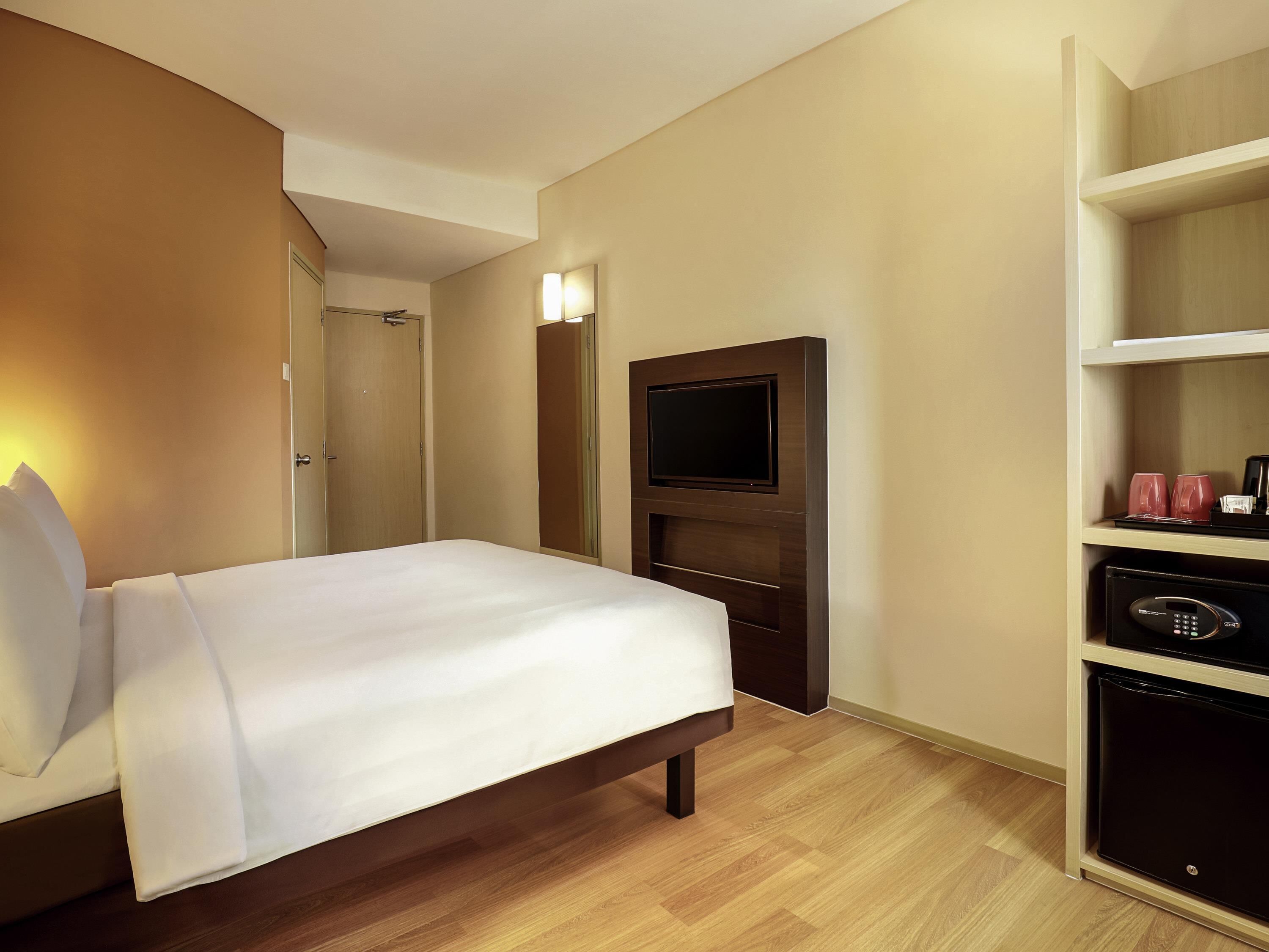 A hotel room with a bed, a TV mounted on the wall, and a minibar.