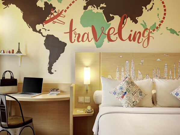 A hotel room with a world map wall art, a laptop on the desk, and a bed with cityscape pillows. - Ibis Jakarta Harmoni (Jakarta)