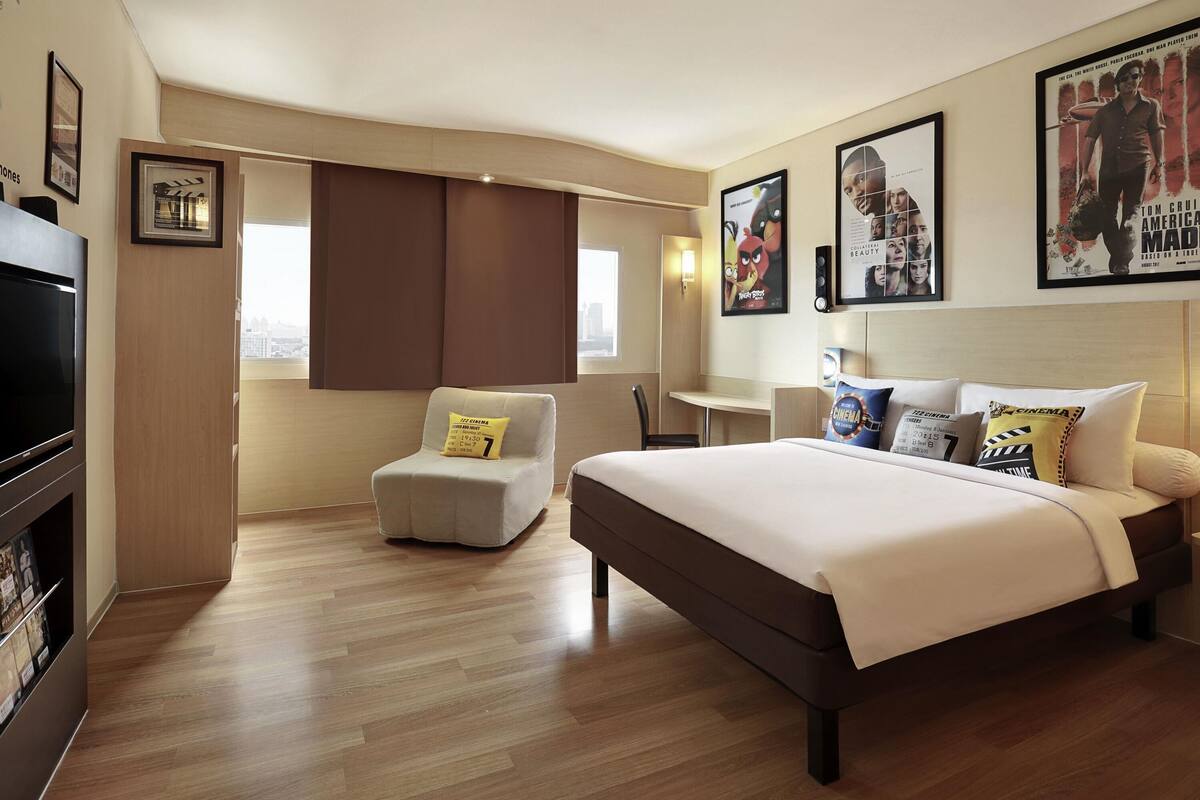 Habitación de hotel con cama, escritorio, silla, televisor y carteles de películas en la pared.
