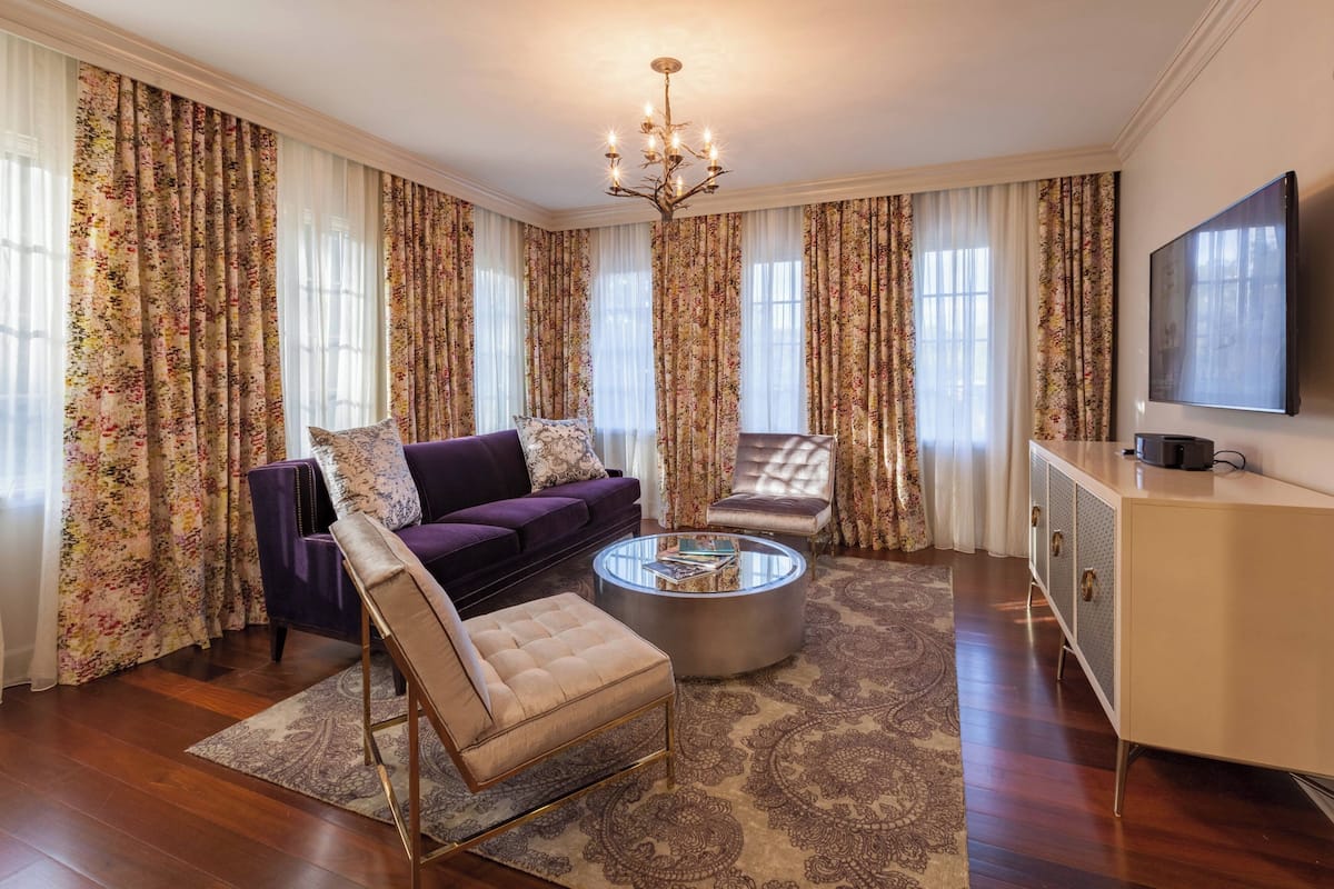 Un salon avec un canapé violet, un fauteuil beige, une table basse ronde et un téléviseur posé sur un meuble.