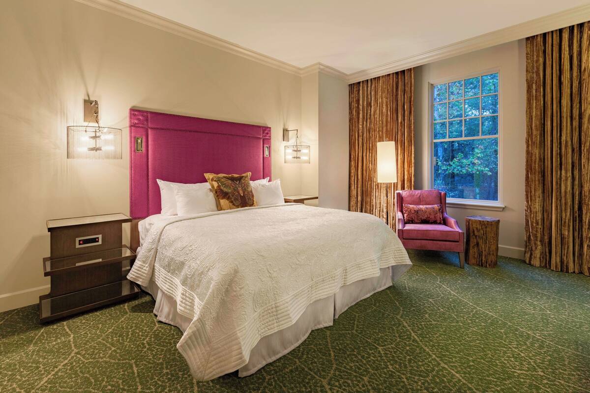 Une chambre d’hôtel avec un grand lit, une table de chevet, une chaise et une fenêtre avec des rideaux.