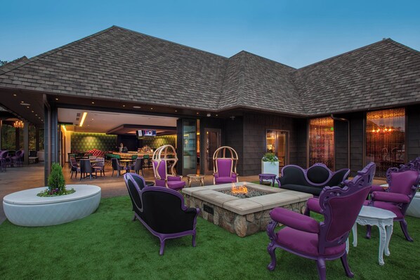 Ein Terrassenbereich im Freien mit einem Feuerkorb, violetten Stühlen und einem Esstisch.