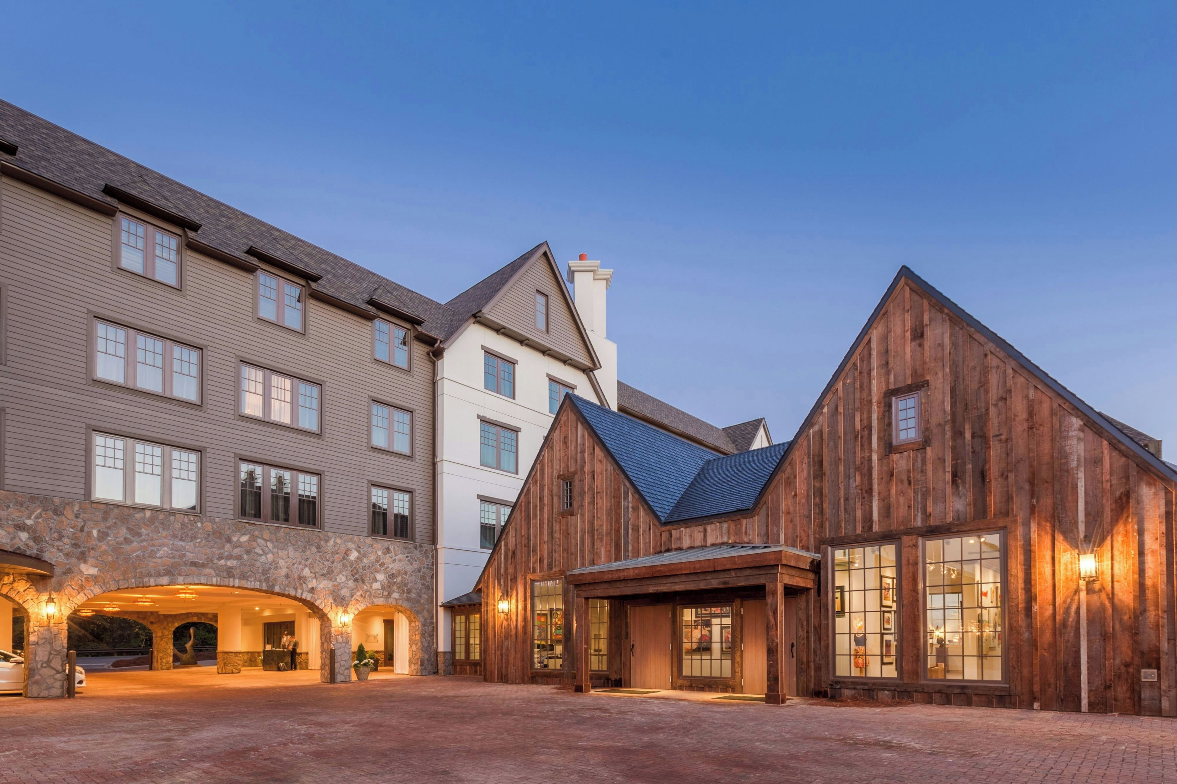 A hotel with a stone facade, a wooden building with a sloped roof, and a paved courtyard.