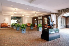A lobby with a brick floor, potted plants, a statue, and a stone wall.