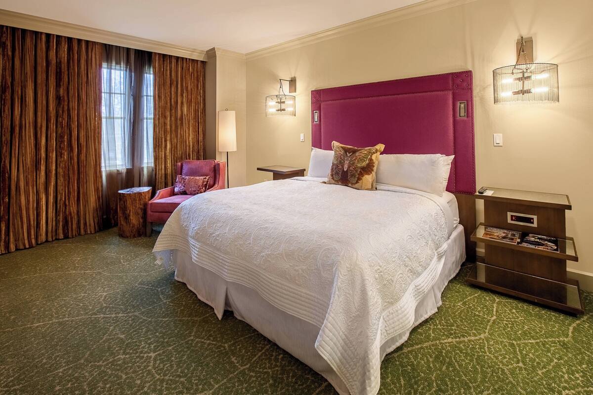 Une chambre d’hôtel avec un grand lit, une chaise, une table de chevet et une lampe.