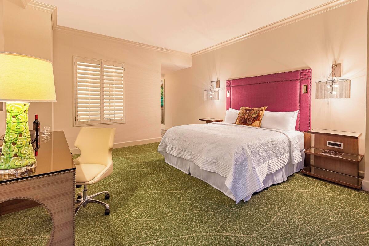 Une chambre d’hôtel comprenant un lit, un bureau avec une lampe, une chaise et une table de chevet.