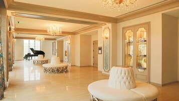 Um hall amplo e ricamente decorado, com um piano de cauda, lustres ornamentados e áreas de estar confortáveis.