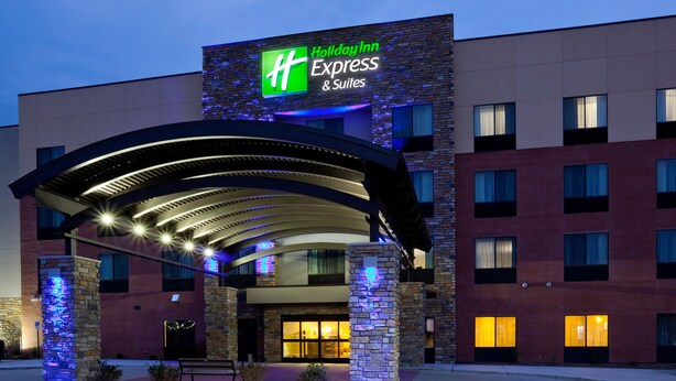 A Holiday Inn Express & Suites building with a brick facade, a covered entrance, and illuminated signage.