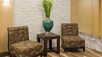 A seating area with two upholstered chairs and a small table, a decorative vase with green foliage, and a textured wall.