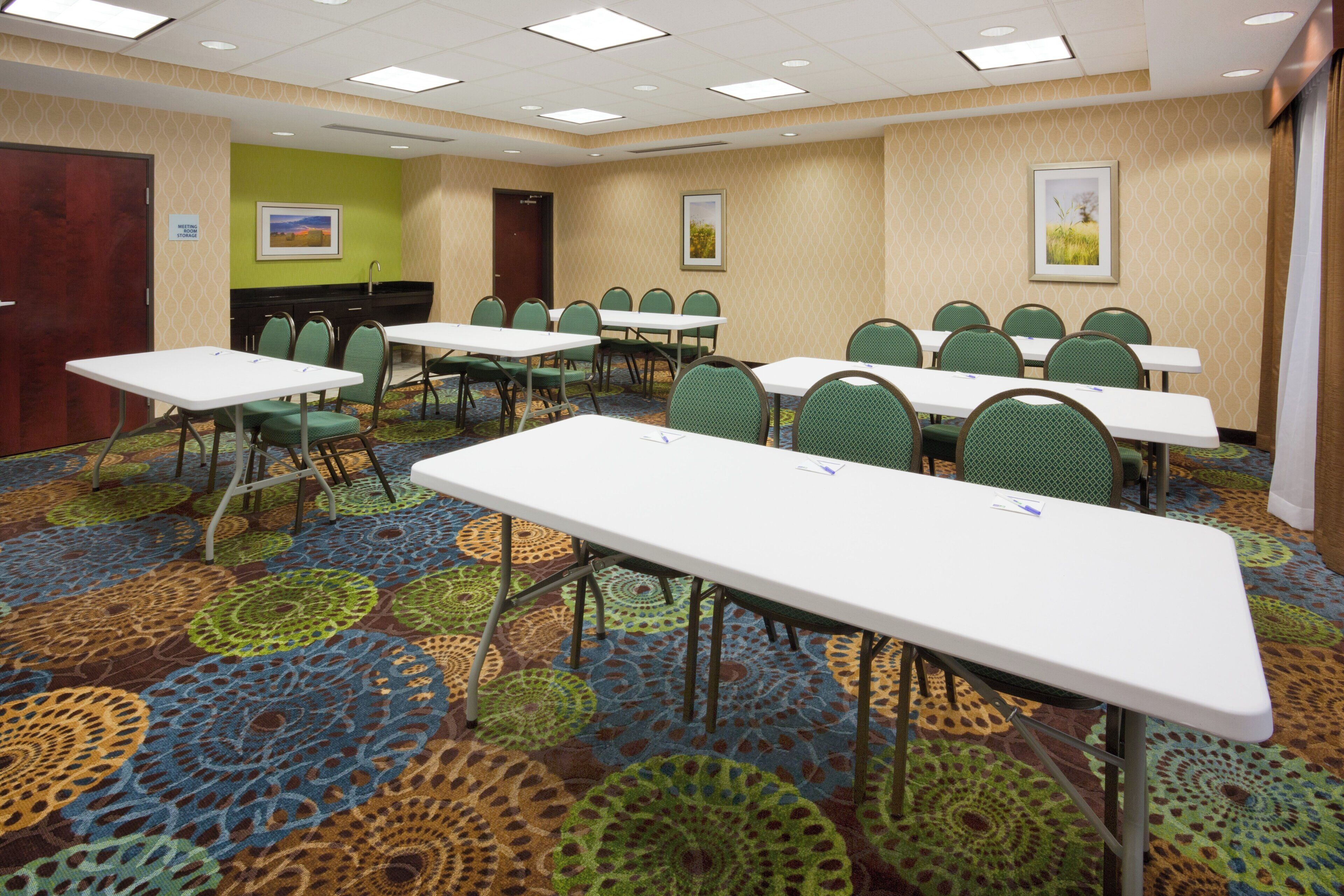 Un salón de conferencias de hotel con múltiples mesas y sillas, alfombra estampada y una pared de acento verde.