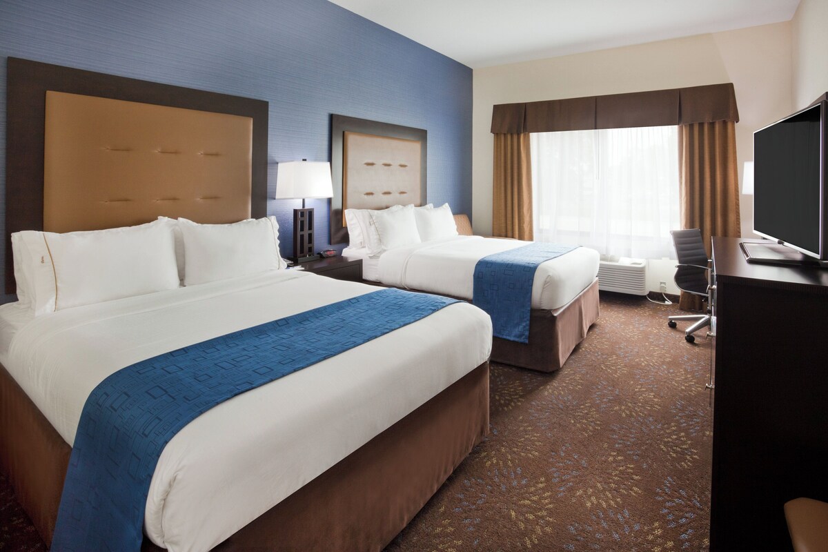 A hotel room with two beds, a desk, a chair, and a television.