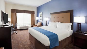 A hotel room with a large bed, a desk with a computer, a chair, a lamp, and a window with curtains.