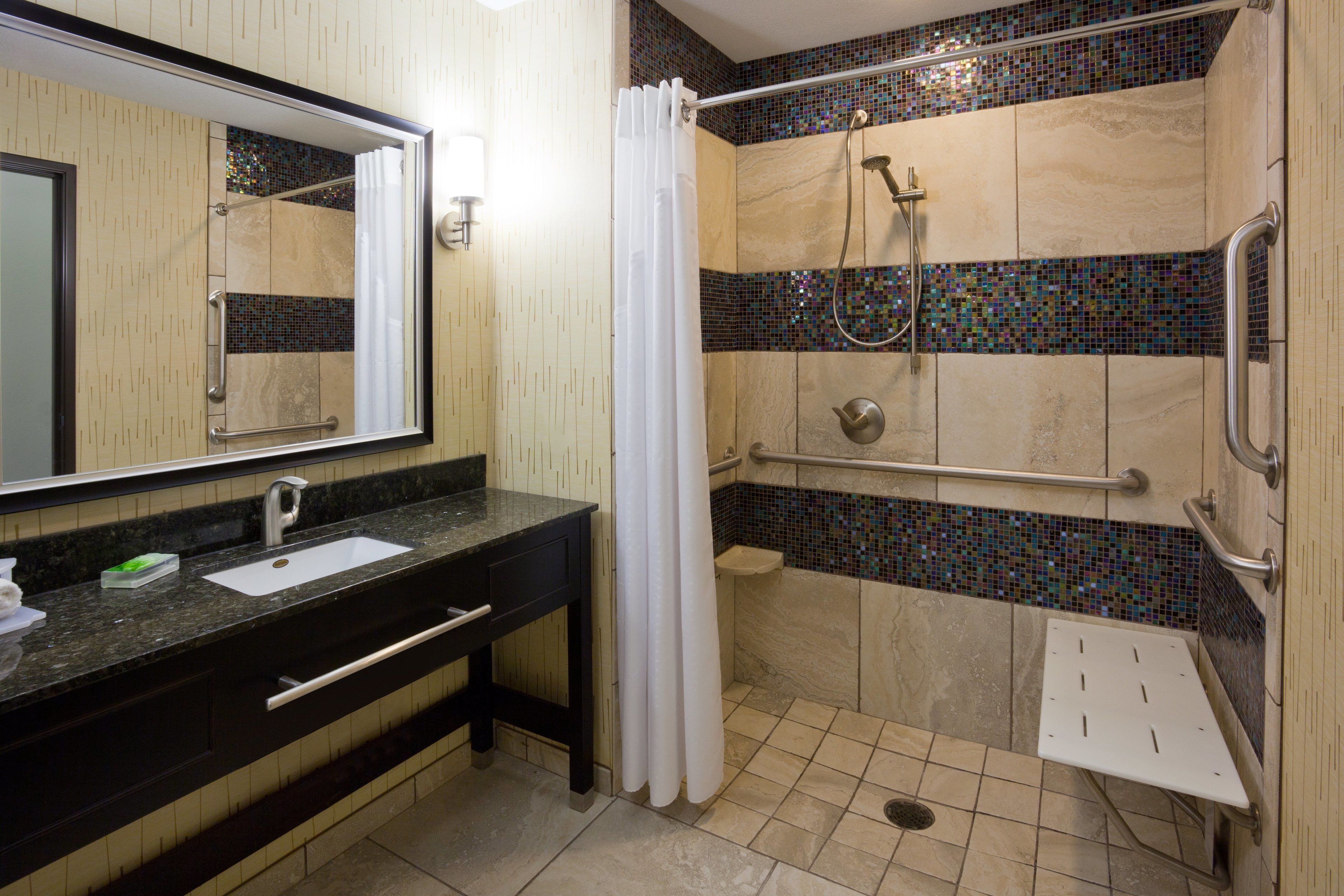 A modern bathroom with a sink, mirror, shower, and grab bars.