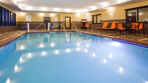 A swimming pool with a tiled edge, adjacent to a seating area with orange chairs and a table. - Holiday Inn Express & Suites Davenport by IHG (Davenport)