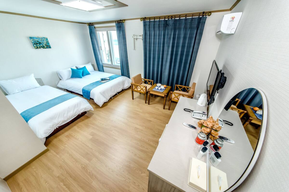 Une chambre d’hôtel avec deux lits, un bureau avec un miroir, une télévision et une fenêtre avec des rideaux.
