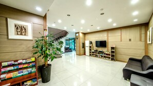A modern lobby with a staircase, a reception desk, a bookshelf, a potted plant, a sofa, and a television.