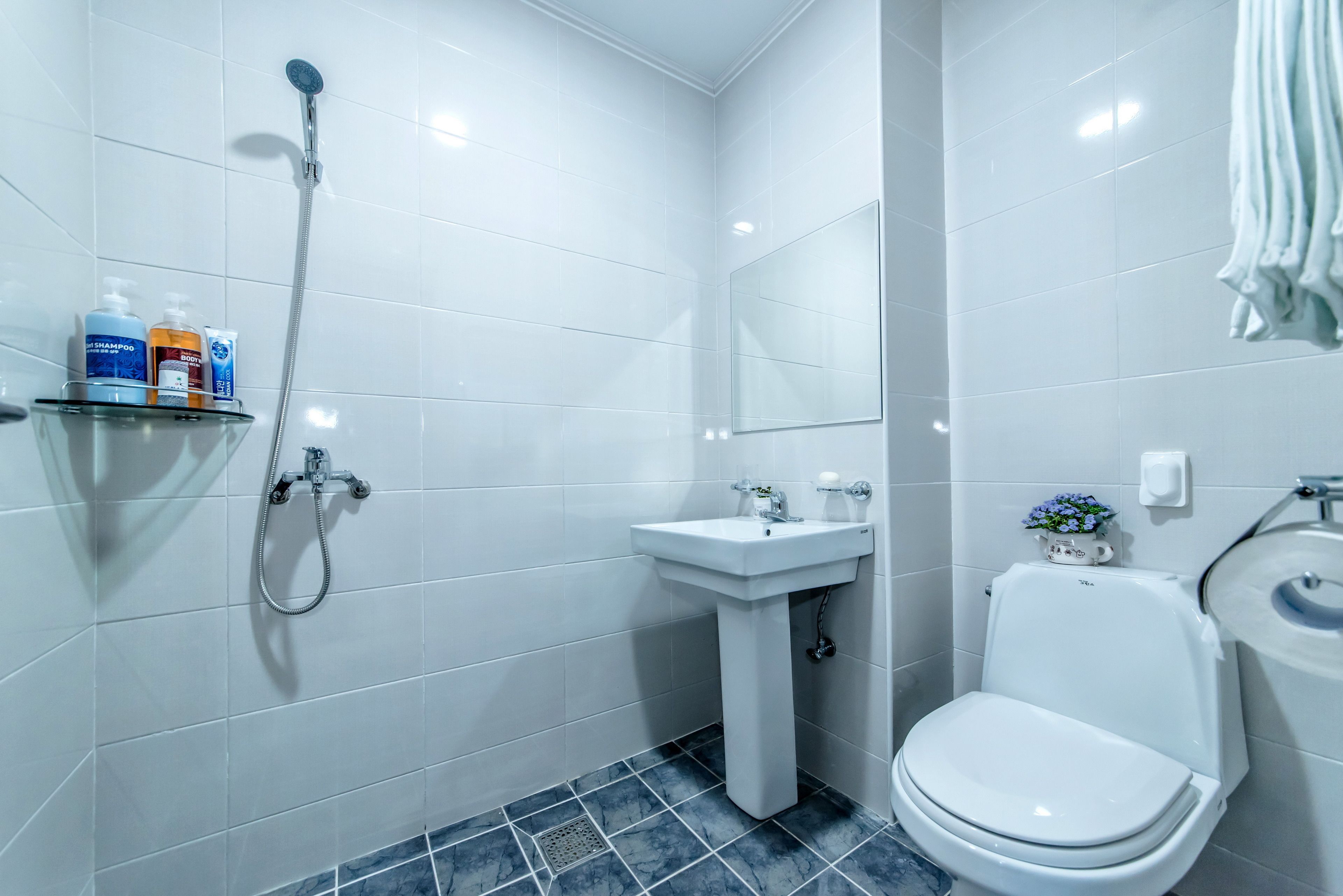 Ein modernes Badezimmer mit weißen Fliesen, einer Dusche, einem Waschbecken und einer Toilette.