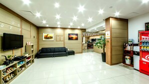 A modern living room with a flat-screen TV, a black sofa, wooden paneling, a painting, and a vending machine.