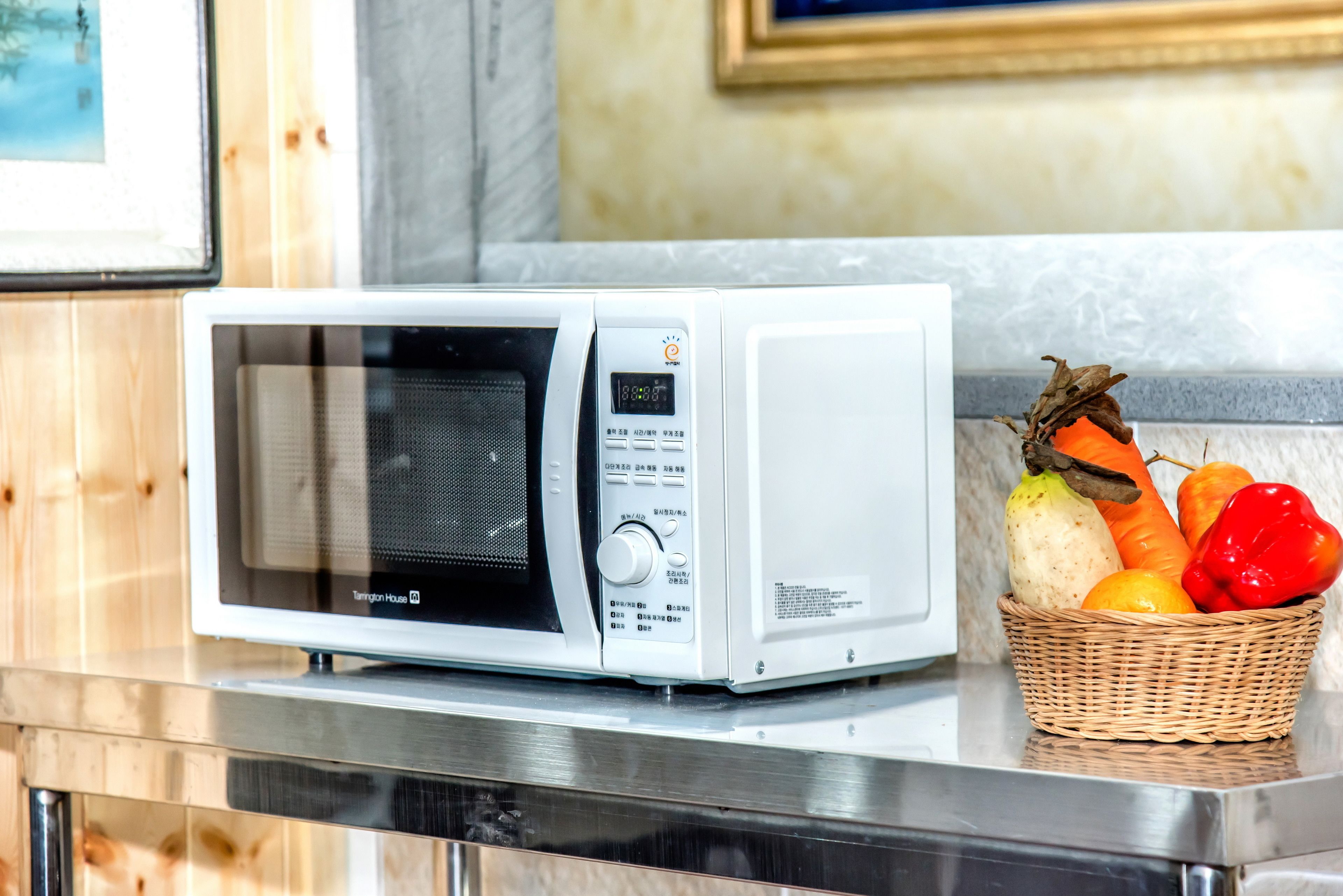 A microwave oven on a kitchen counter with a basket of fruits beside it.