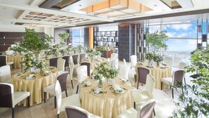 Une salle de banquet spacieuse, avec des tables rondes, des chaises blanches et des centres de table floraux.