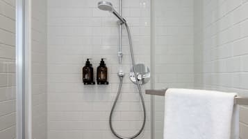 Eine Dusche mit Duschbrause und Wandarmatur. Auf einem Regal stehen zwei Flaschen Shampoo und Conditioner. Ein weißes Handtuch hängt an einem Ablagegestell.