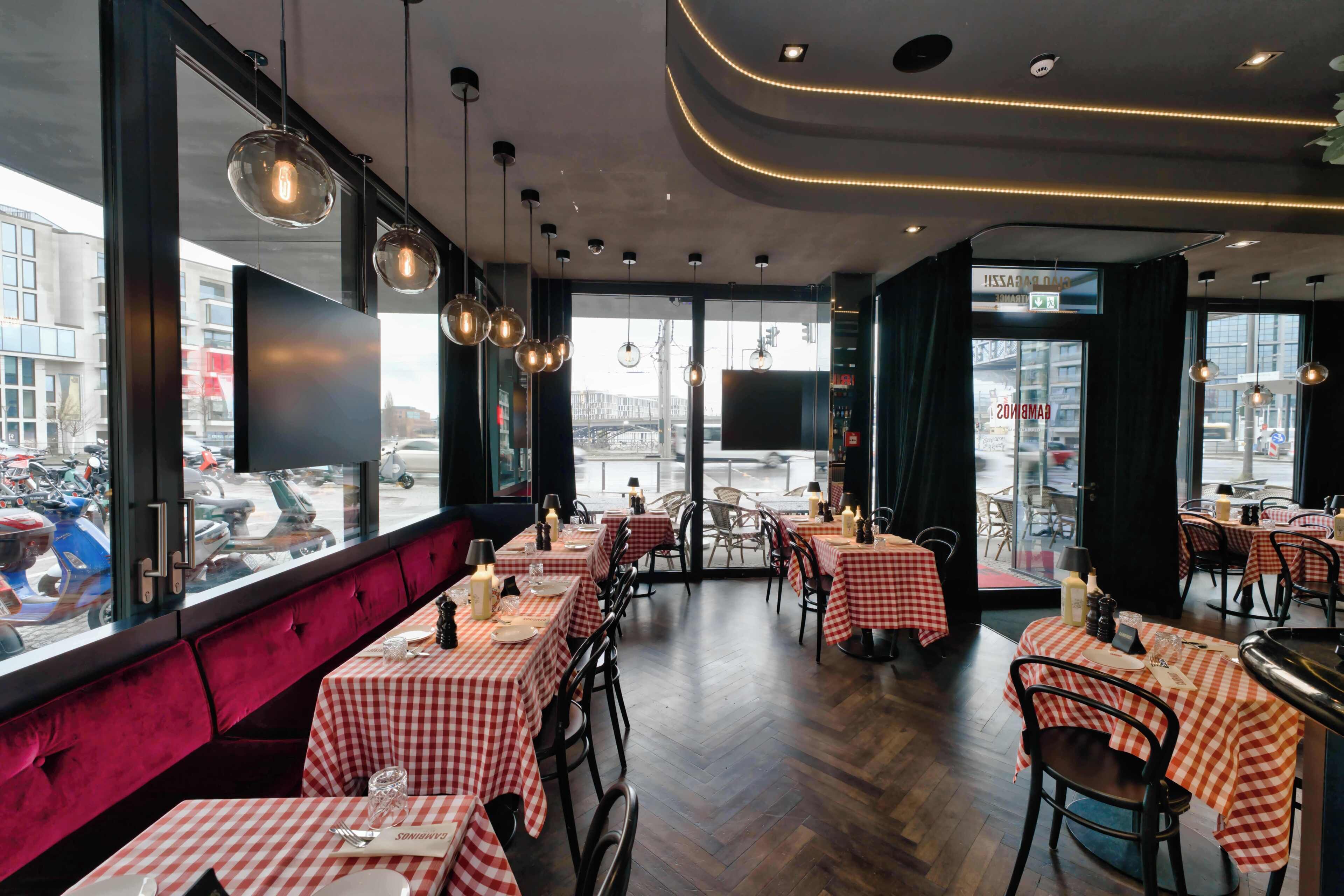 Un ristorante con tovaglie a quadri, illuminazione a sospensione e vista sulla strada attraverso ampie finestre.