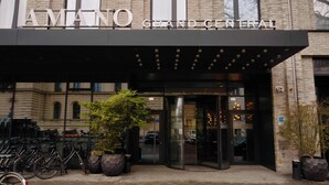 The entrance to the AMANO GRAND CENTRAL hotel with a glass door, potted plants, and bicycles parked outside. - Hotel AMANO Grand Central (Berlin)