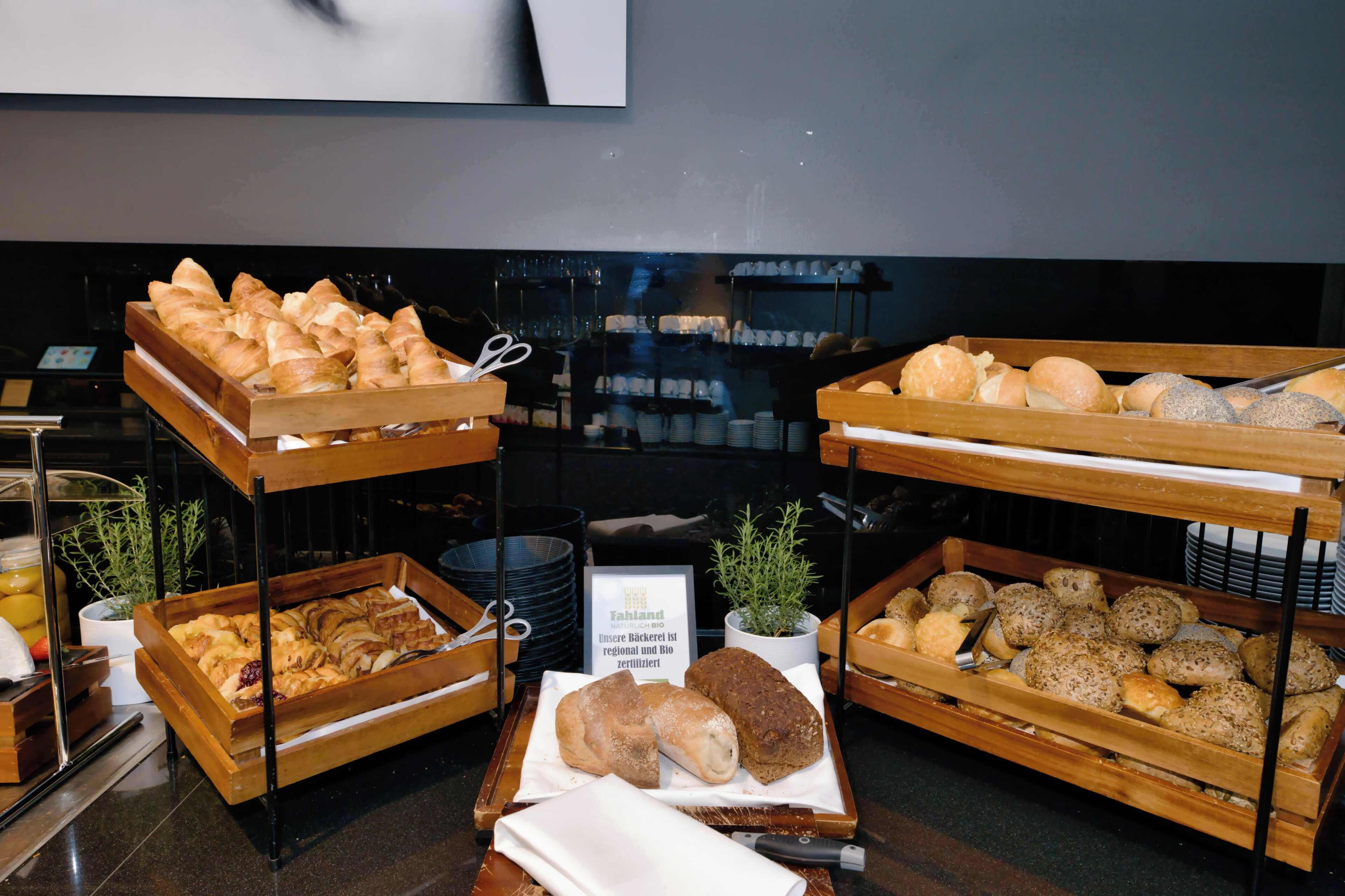 A buffet with various baked goods, including croissants and bread rolls, displayed on wooden stands.