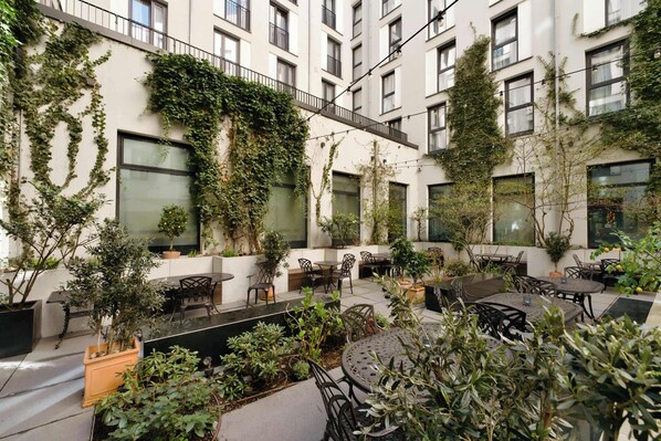 A courtyard with outdoor seating, potted plants, and a building with multiple windows and balconies.