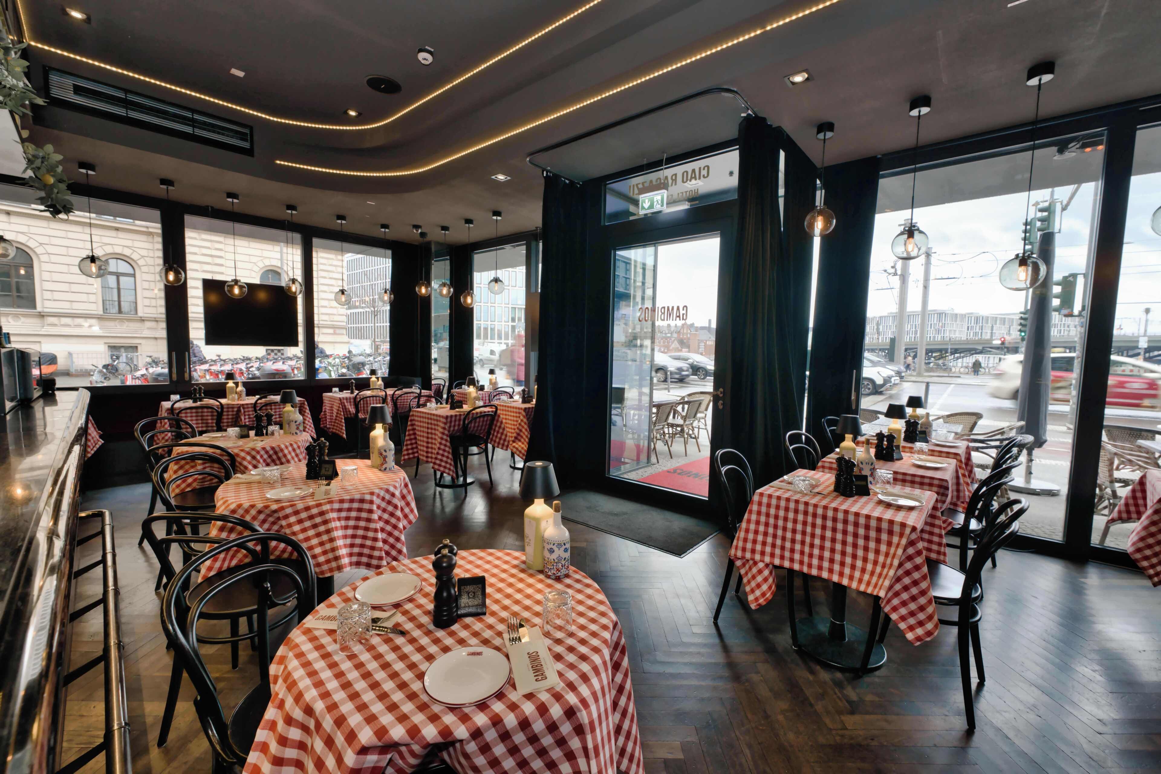 Ein Restaurant mit karierten Tischdecken, runden Tischen und hängenden Pendelleuchten.