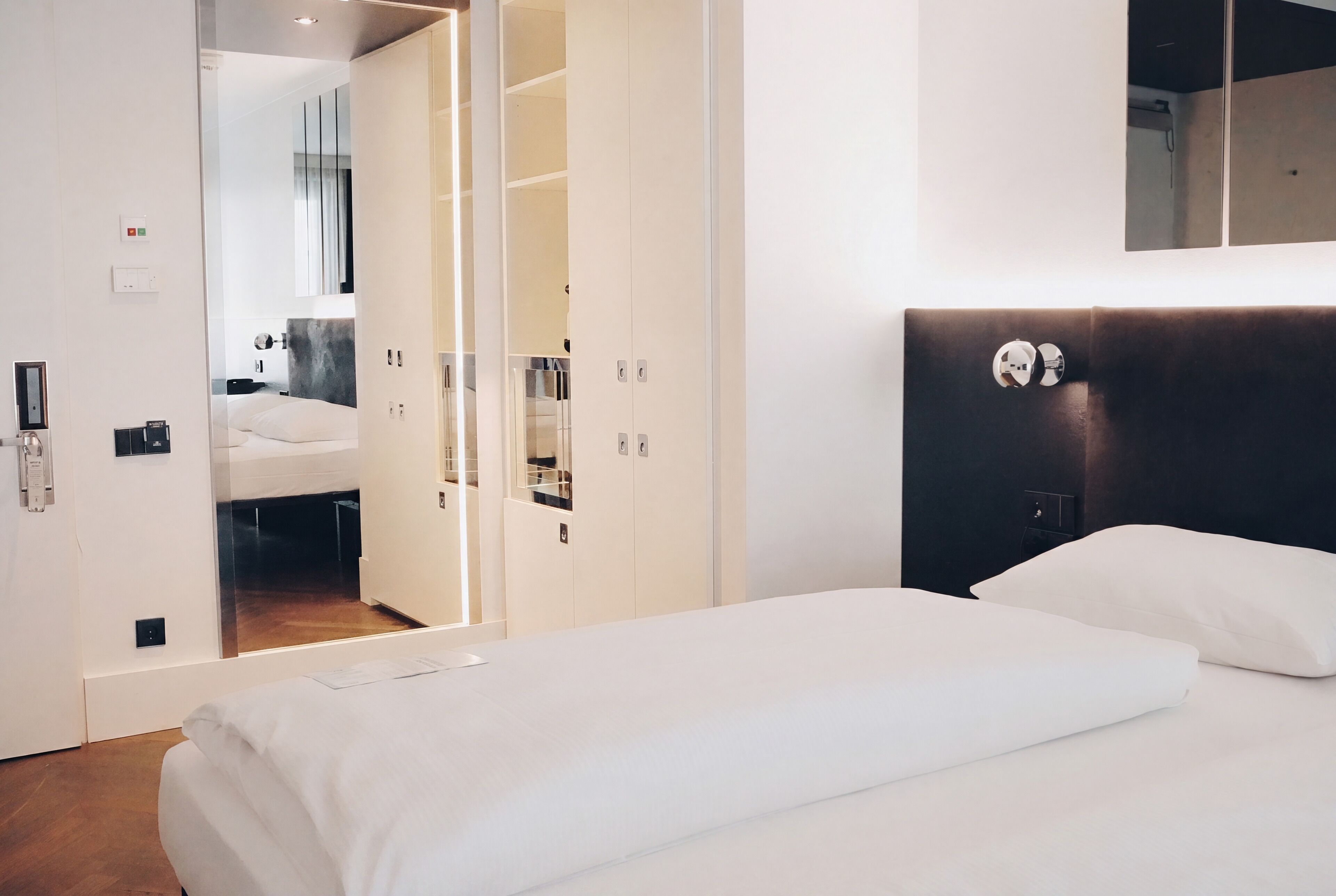 Moderni hotellihuone, jossa on suuri sänky, erillinen vaatehuone ja peili sängyn yläpuolella.