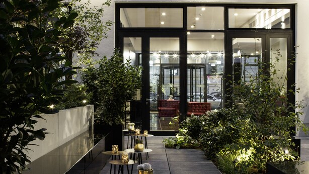A modern building with a courtyard featuring outdoor seating and potted plants. - Hotel AMANO Grand Central (Berlin)